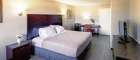 Una habitación de hotel con cama, escritorio, televisor y mesita de noche.