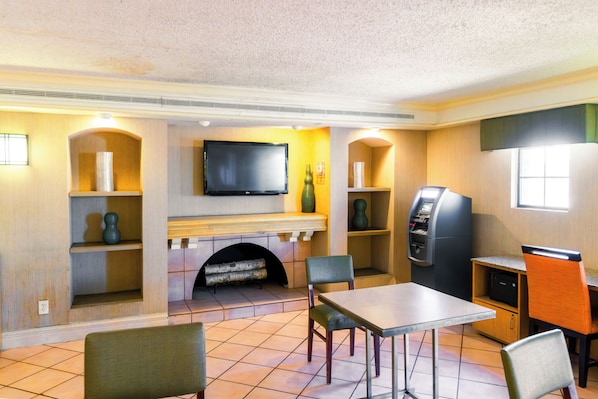 A room with a fireplace, a flat-screen TV, a self-service kiosk, and a table with chairs. - Home Suites Culebra (San Antonio)