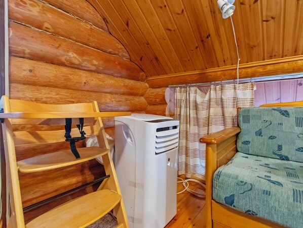 A cabin interior with a bunk bed, a heater, a window with curtains, and a patterned sofa.