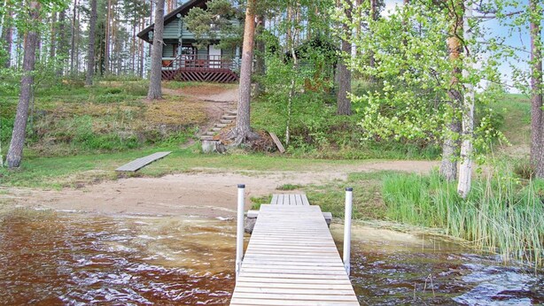 A wooden dock leading to a cabin surrounded by trees.