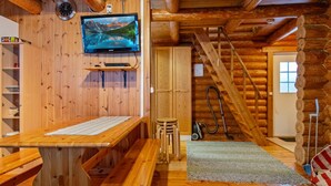 A wooden cabin interior with a wooden staircase, a television mounted on the wall, and a wooden table.