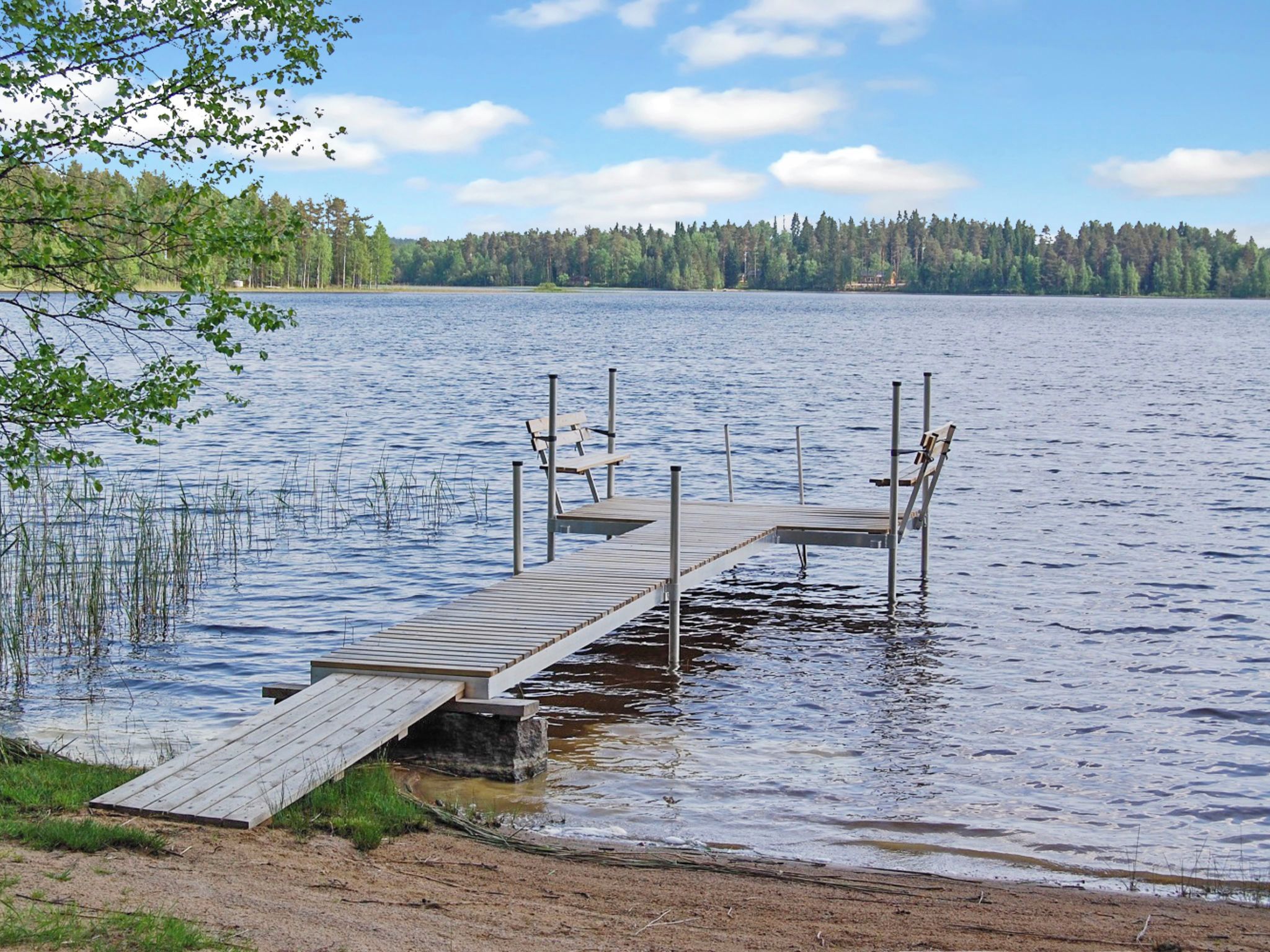 A wooden dock extending into a calm lake with a forested shoreline in the background.