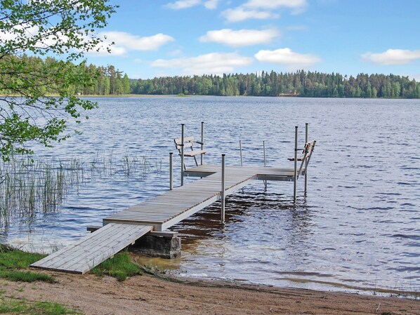 Une jetée en bois s’étendant sur un lac paisible, avec une rive boisée en arrière-plan.