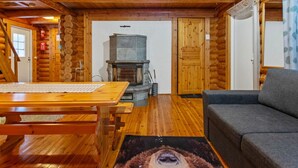 A log cabin interior with a wooden table, a sofa, a fireplace, and a rug with an animal design.