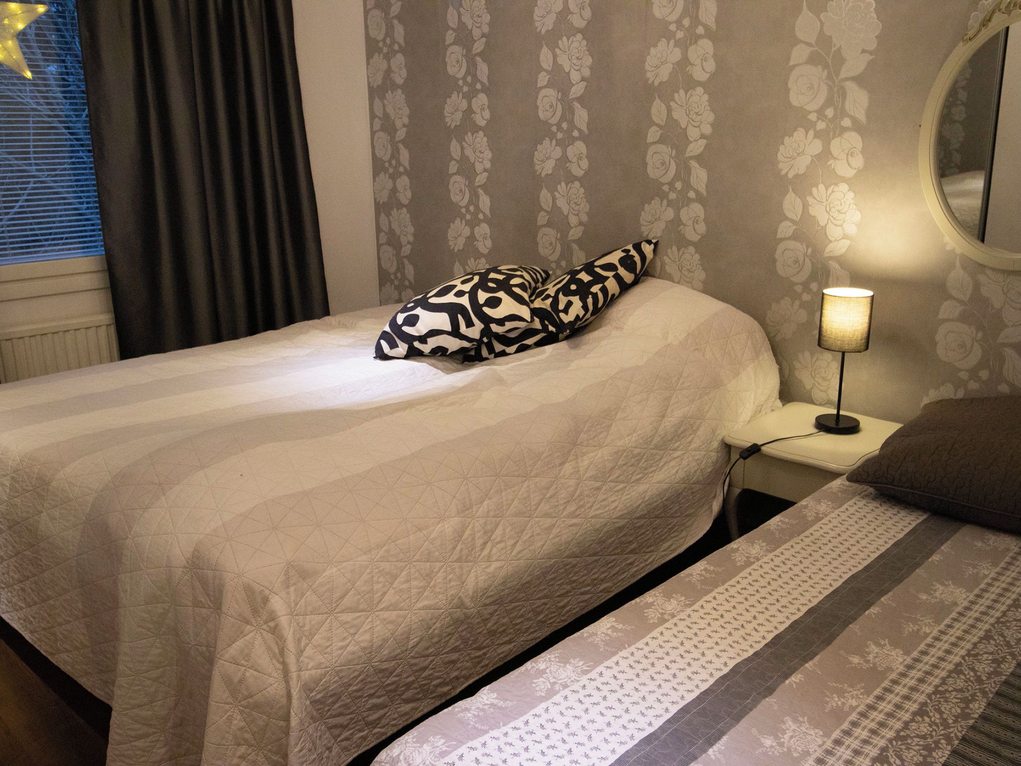 A bedroom with a bed, a bedside table with a lamp, and a window with curtains.