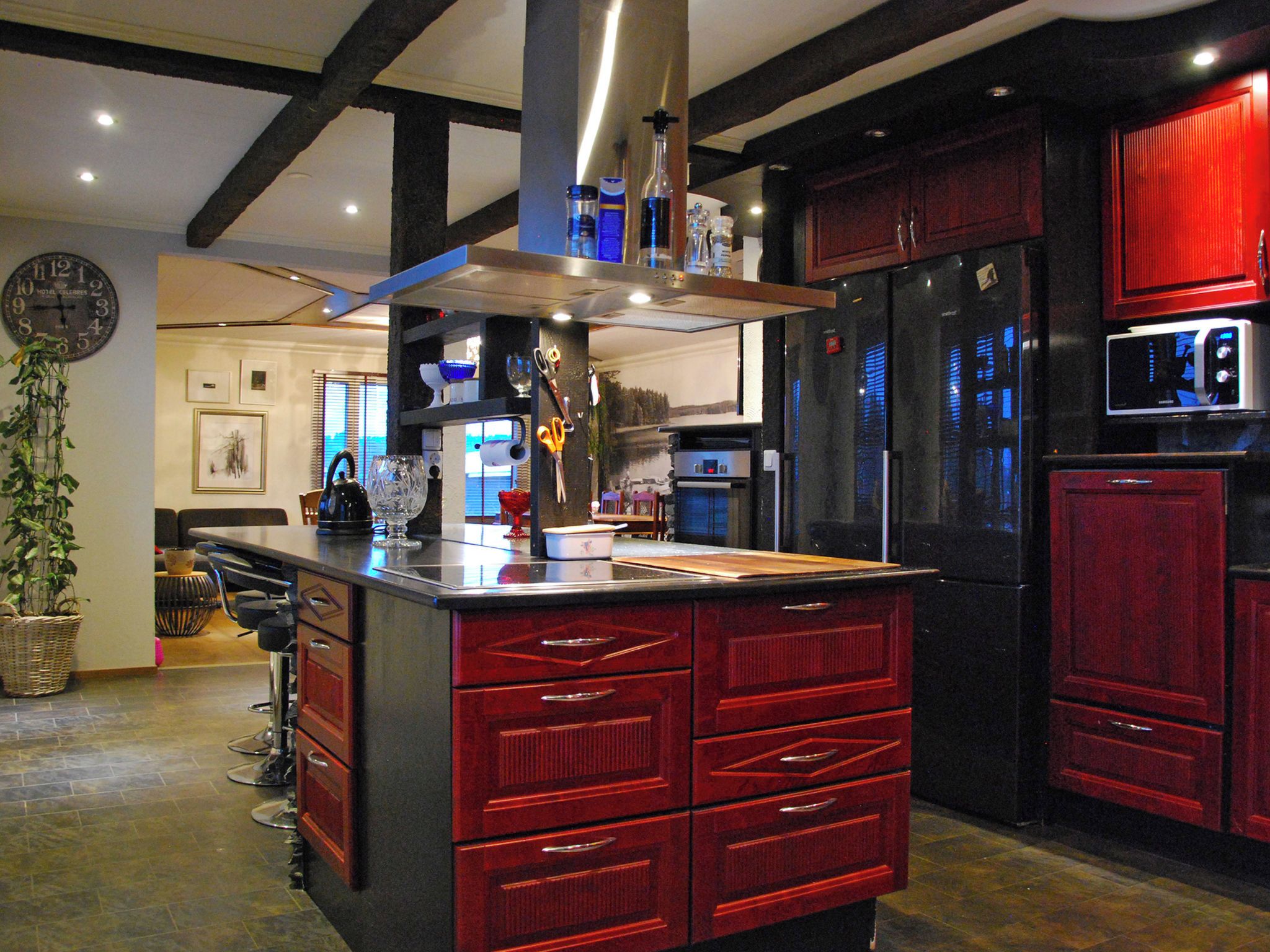 A modern kitchen with a central island, red cabinetry, and stainless steel appliances.