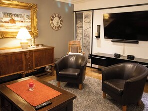 A living room with a wooden cabinet, two leather armchairs, a red rug, a remote control, a painting, a clock, and a flat-screen TV. - Villa meka by Interhome (Sastamala)
