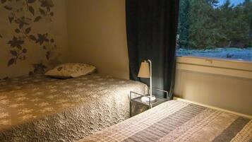 A bedroom with a bed, a bedside table with a lamp, and a window with a view of trees.
