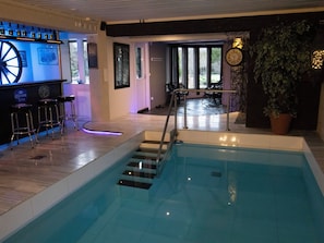 An indoor swimming pool with a glass barrier, bar area with stools, and a clock on the wall. - Villa meka by Interhome (Sastamala)