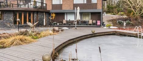 Una casa moderna de dos pisos con un patio que incluye un pequeño estanque y zona de estar.