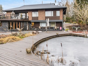 A modern two-story house with a patio area featuring a small pond and seating.