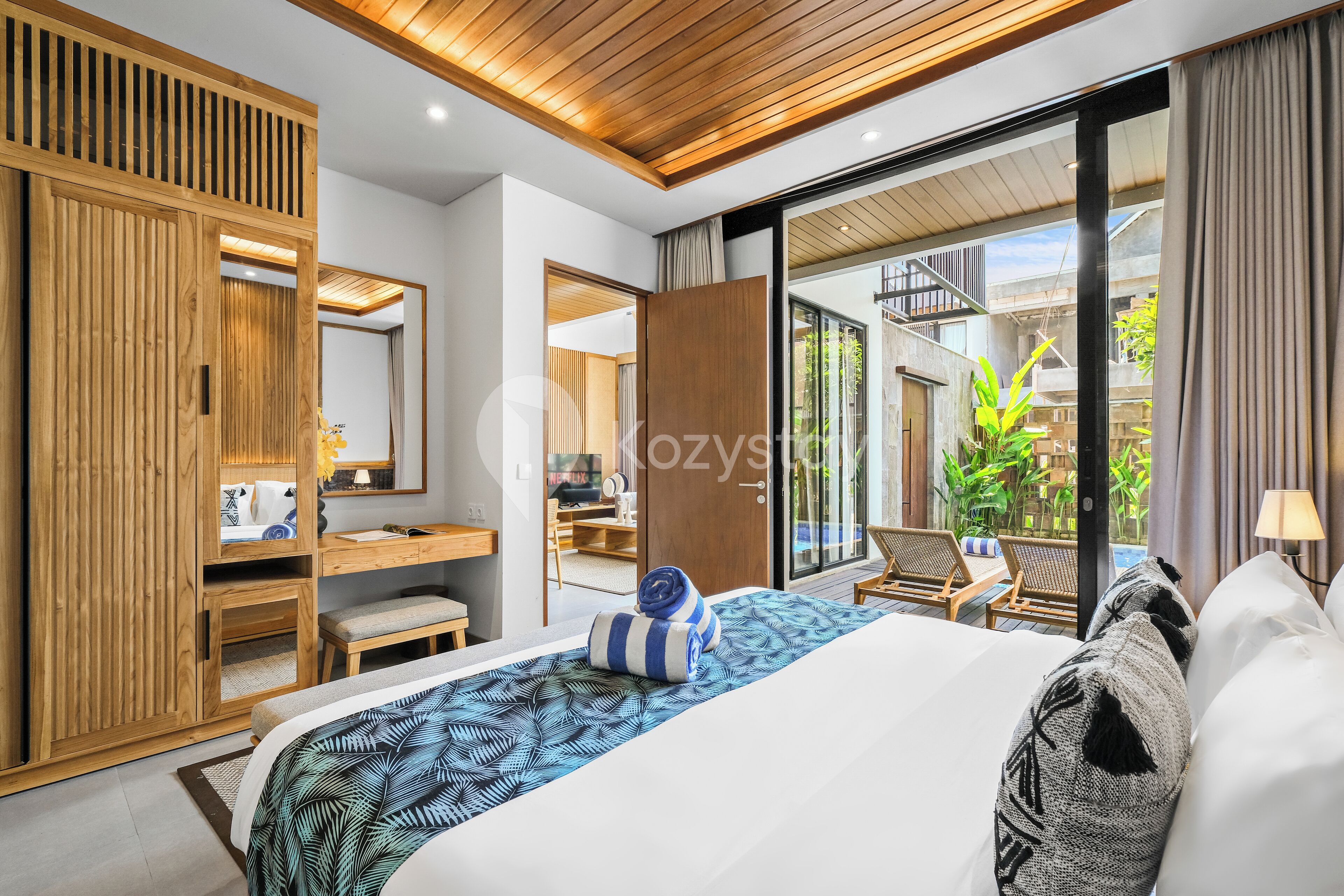 Ein modernes Hotelzimmer mit Bett, einem Holzschrank, einem Schreibtisch und einem Balkon mit Blick auf Grünflächen.
