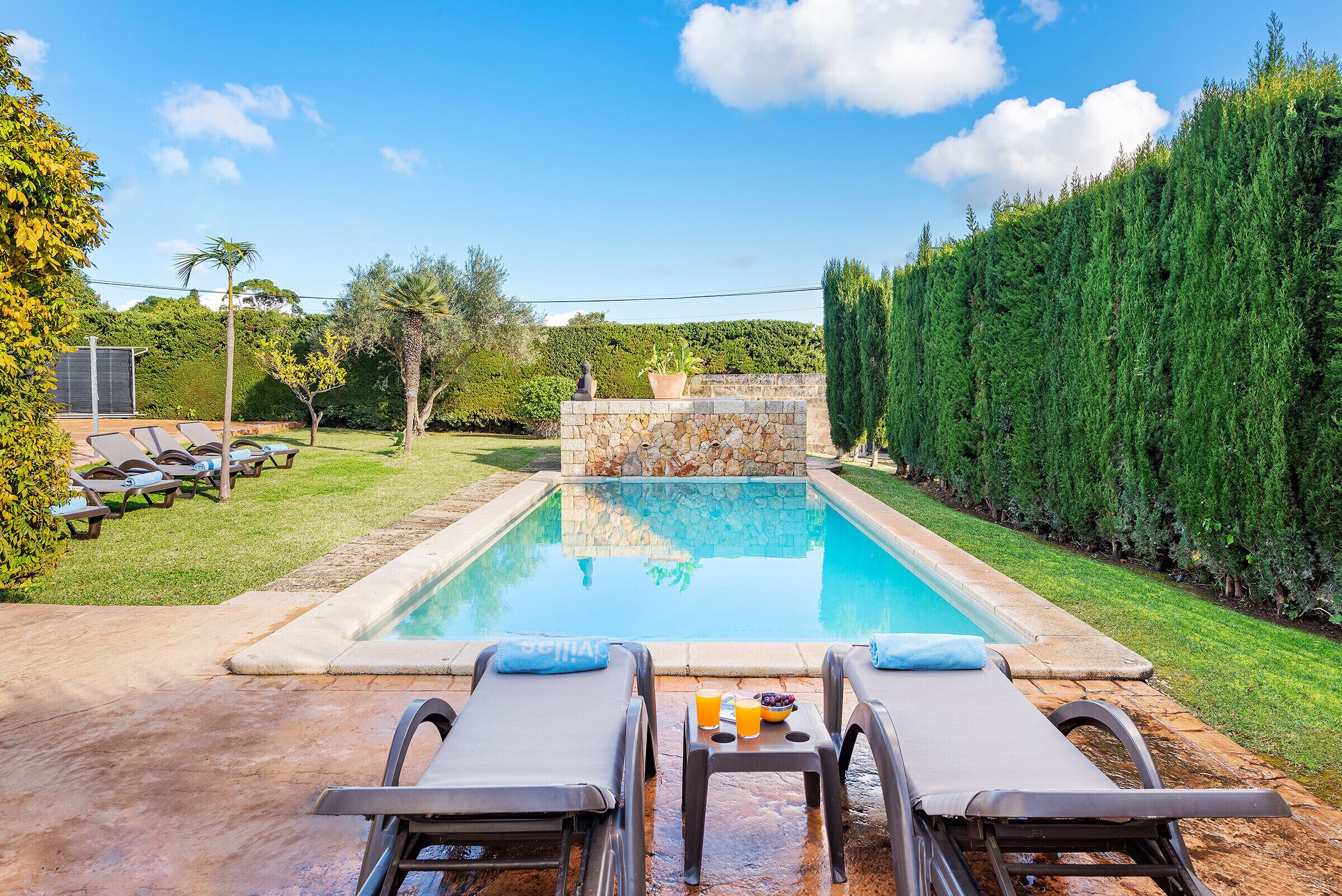 Une piscine avec des chaises longues et un mur en pierre.