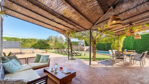 Eine Terrasse im Freien mit Holztisch, gepolsterten Sitzgelegenheiten und hängenden Korblampen.