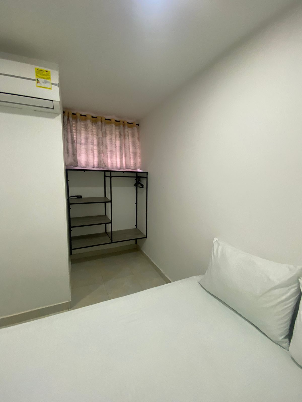 Una habitación pequeña y sencilla con cama, armario empotrado con espejo y ventana con cortinas.