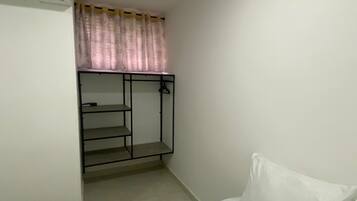 Una habitación pequeña y sencilla con cama, armario empotrado con espejo y ventana con cortinas.