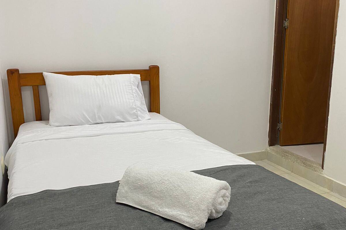 A single bed with a wooden headboard, white bedding, and a grey blanket.
