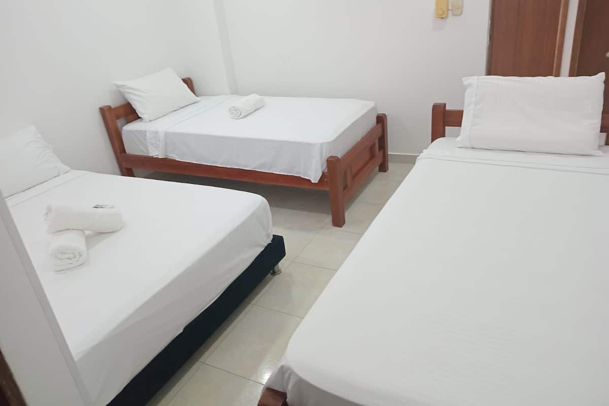 A hotel room with two single beds, each with white linens and pillows, wooden headboards, and a tiled floor.