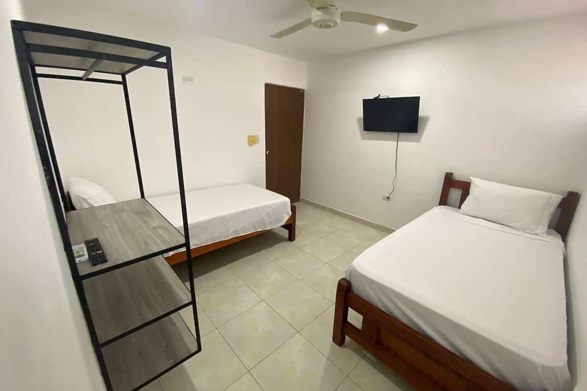 A bedroom with a bed, a desk with a chair, a ceiling fan, and a TV on the wall.