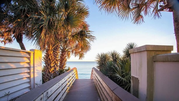 A wooden boardwalk leading to a beach with palm trees and a clear sky.