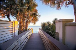 A wooden boardwalk leading to a beach with palm trees and a clear sky.