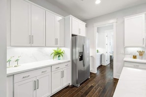 A modern kitchen with white cabinets, a stainless steel refrigerator, and a wooden floor.