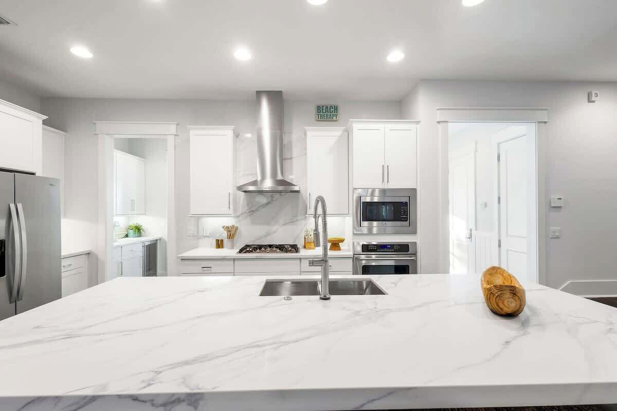 A modern kitchen with white cabinetry, a stainless steel range hood, a microwave, and a built-in oven.