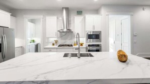 A modern kitchen with white cabinetry, a stainless steel range hood, a microwave, and a built-in oven.