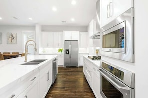 A modern kitchen with white cabinetry, stainless steel appliances, and a wooden floor.