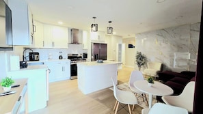A modern kitchen with white cabinets, a central island, and a dining area with white chairs and a table.