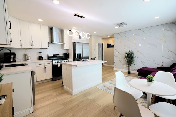 A modern kitchen with white cabinets, a central island, and a dining area with white chairs and a small table.