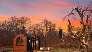 Eine Holzhütte mit einem Satteldach, einer Terrasse mit Stühlen und einem Baum mit Lichterketten.