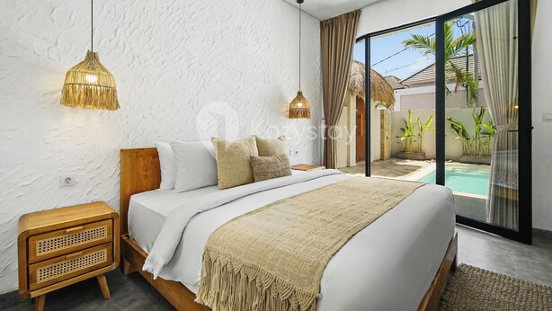 A modern bedroom with a large bed, two bedside tables, and a view of a swimming pool through glass doors. - Kalea Villa by Kozystay - Ungasan (Ungasan)