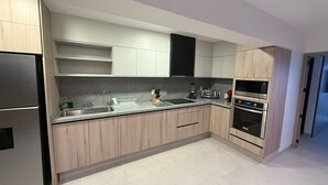 Eine moderne Küche mit hellen Holzschränken, einem Edelstahlkühlschrank, einem eingebauten Backofen und einer Mikrowelle.