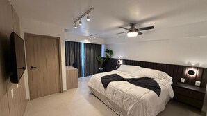 Ein modernes Schlafzimmer mit einem großen Bett, einem Deckenventilator, Einbauleuchten, einem an der Wand montierten Fernseher und einem Holzschrank.