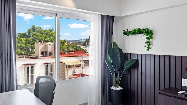 Ein modernes Zimmer mit großem Fenster, einer Zimmerpflanze, einem Schreibtisch und einem Stuhl.