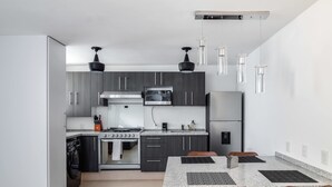 A modern kitchen with dark cabinets, a granite countertop, a built-in oven, a microwave, and a stainless steel refrigerator. There is a dining table with four chairs and pendant lights above it. - +MS +Deslumbrante +Suite Centrico +A11 (Santiago de Querétaro)