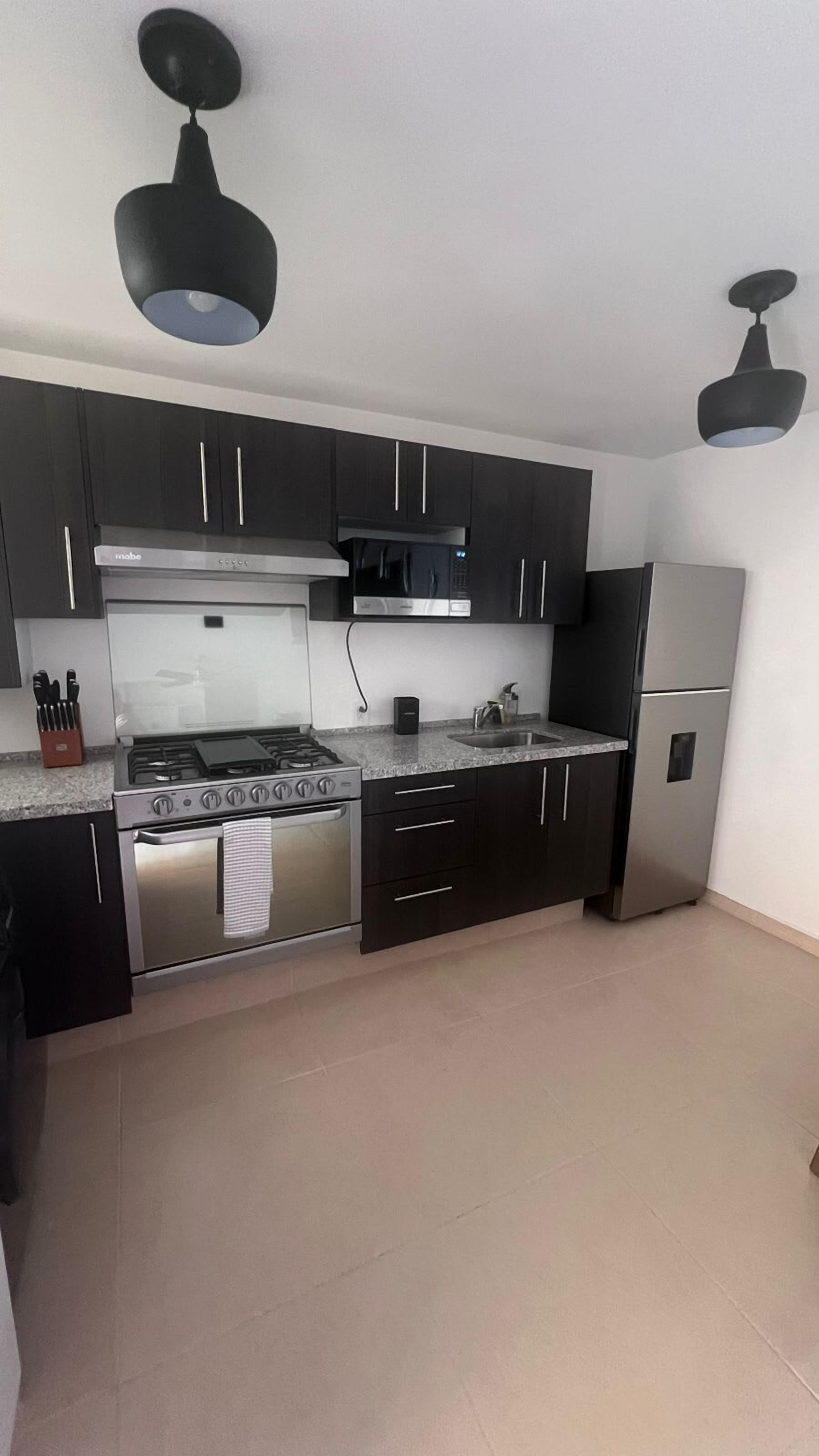Una cocina moderna con armarios oscuros, electrodomésticos de acero inoxidable e iluminación colgante.