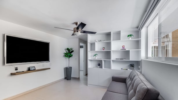 A modern living room with a large flat-screen TV, a ceiling fan, built-in shelving, and a grey sofa. - +MS +Deslumbrante +Suite Centrico +A11 (Santiago de Querétaro)