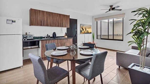 A modern kitchen with wooden cabinets, a dining table set for four, and a large window offering a view. - Ms Magnifica Suite Ubicadisima (Santiago de Querétaro)