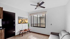 A living room with a sofa, a dining table with chairs, a ceiling fan, a window with a view, and a door. - Ms Magnifica Suite Ubicadisima (Santiago de Querétaro)