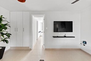 A modern living room with a TV mounted on the wall, a potted plant, and a doorway leading to another room.