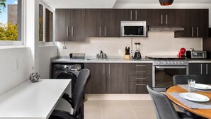 A modern kitchen with dark wood cabinets, a stainless steel stove, a microwave, and a dining area with a table and chairs. - MS  Iluminada Suite Ubicadisima (Santiago de Querétaro)