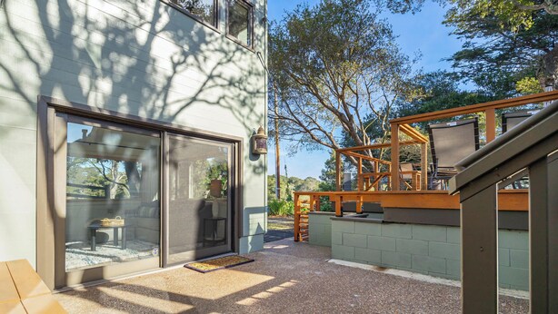 Un patio con piso de madera, puerta de vidrio y vistas a los árboles circundantes.
