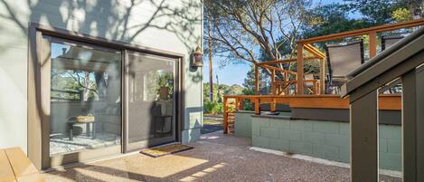 Un espace patio doté d’une terrasse en bois, d’une porte-fenêtre et d’une vue sur les arbres environnants.