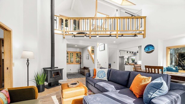 A spacious living area with a high ceiling, a built-in wood-burning stove, a comfortable sofa set, and a staircase leading to an upper level. - Relaxing Getaway Overlooking Schwan Lagoon (Santa Cruz)