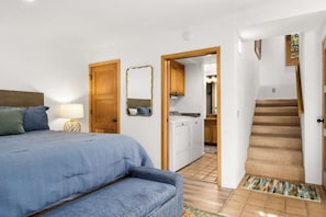 A bedroom with a bed, a nightstand, a lamp, a mirror, and a door leading to a bathroom and kitchen. - Relaxing Getaway Overlooking Schwan Lagoon (Santa Cruz)