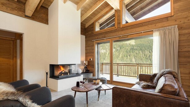 Una sala de estar acogedora con chimenea, asientos cómodos y ventanas amplias con vistas al bosque.