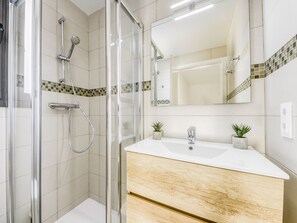 Bathroom features a glass-enclosed shower, handheld showerhead, and wall-mounted faucet.