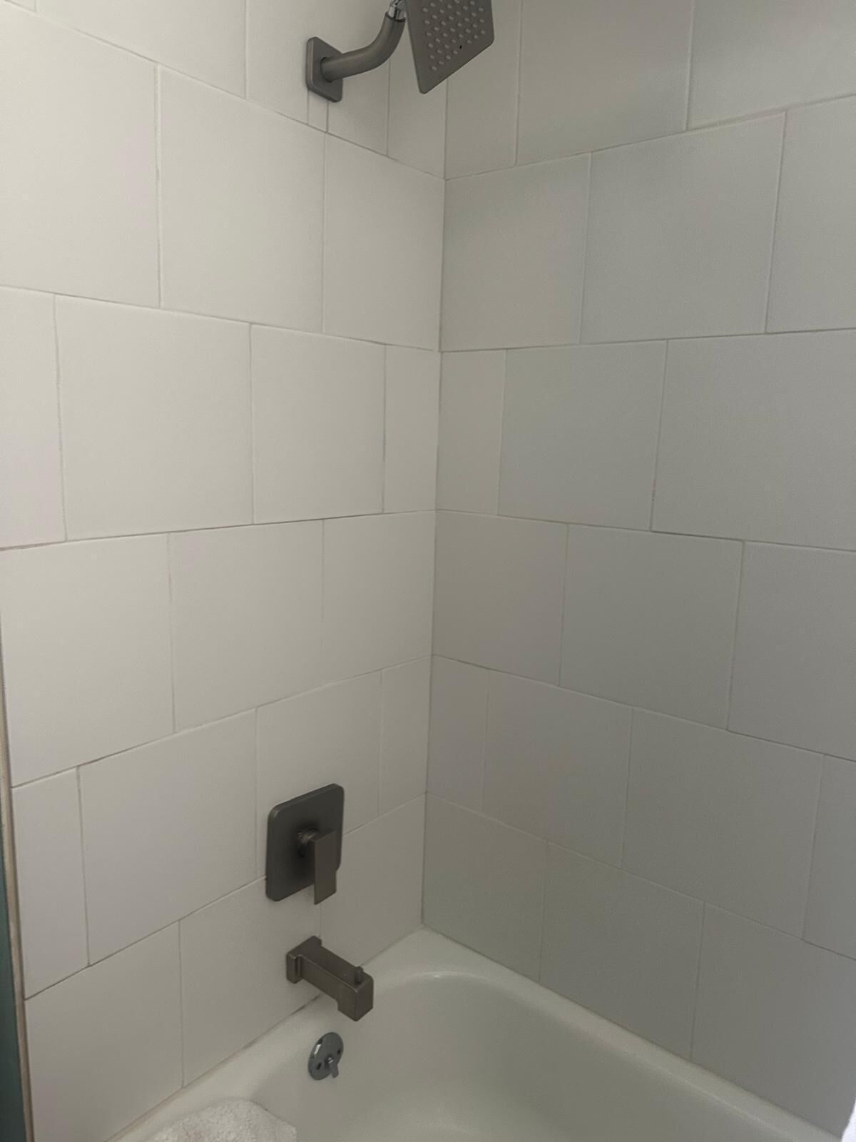 Un baño con azulejos blancos, cabezal de ducha, bañera y retrete.